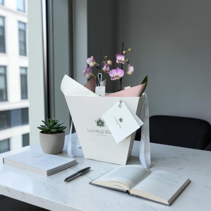 Orquídea lila dentro del empaque blanco estructurado de La Orquídea, con tarjeta y papel de seda
